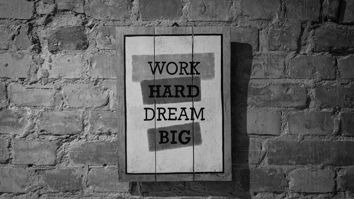 Black and white frame with inspirational Work Hard Dream Big inscription hanging on brick wall